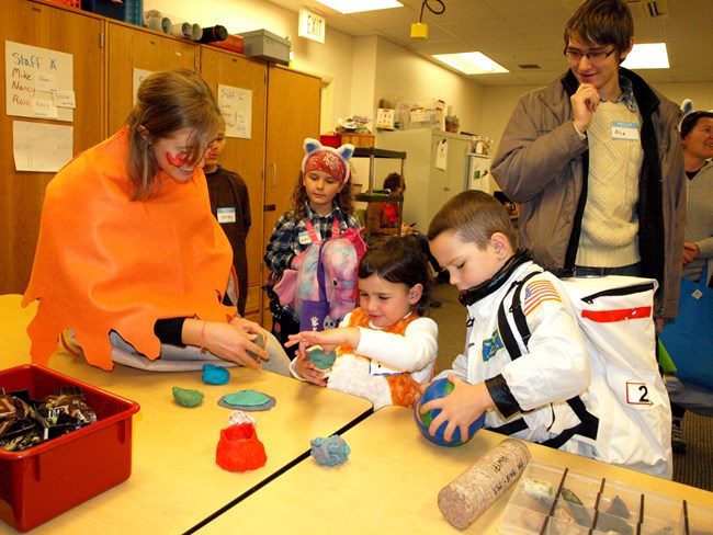 A group of children in costumes gather around a table with clay