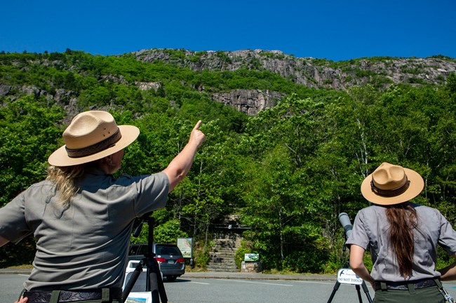 a ranger points at a cliffside