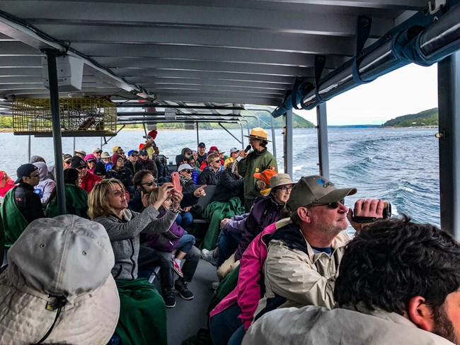 ranger talks into a microphone on a boat while visitors take pictures