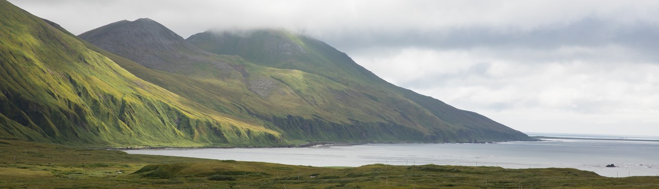 verdant mountain foothills slope down toward coastal waters.