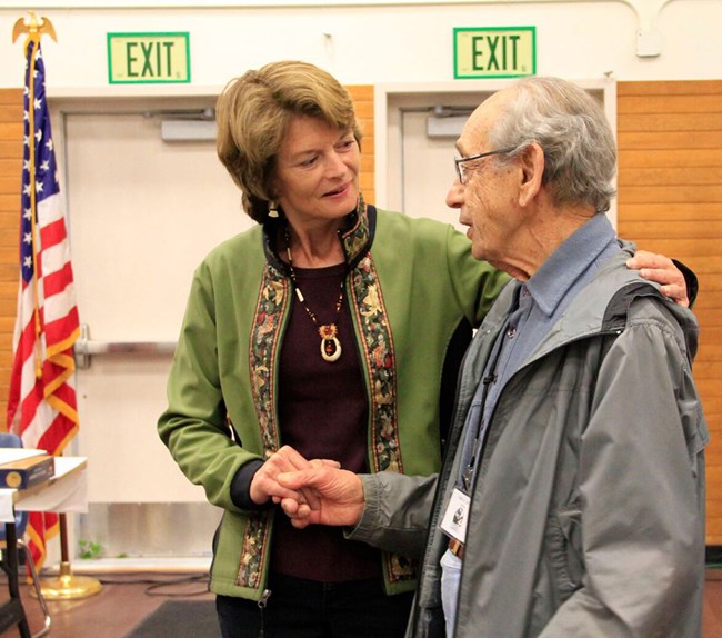 A woman shakes hands with an older man.