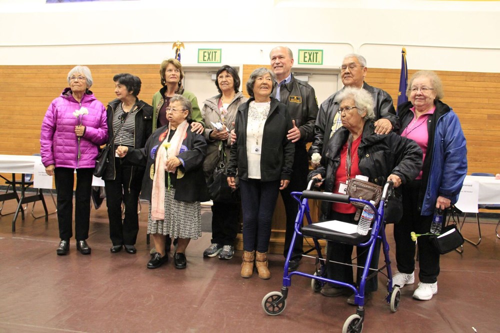 Eleven people pose for a photo in front of flags.