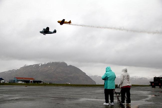 Two people watch historic planes fly across a cloudy sky