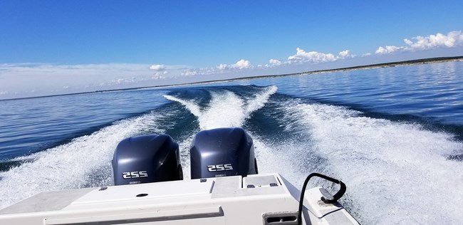 Back of motorboat looking out toward the horizon showing a banking turn to the starboard side.