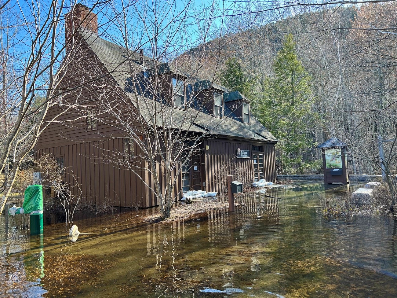 Brown building with sandbags in front of its two sets of doors, surrounded by water.