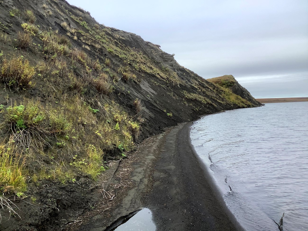 photo of a lake shore with narrow beach and steep bank