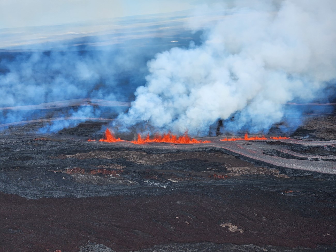 aerial view of volcano erupting with red lava and clouds of ash