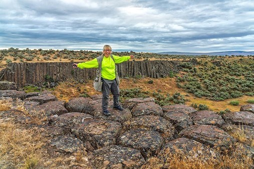 Woman stands on geometric shaped rocks with blue sky and clouds in background