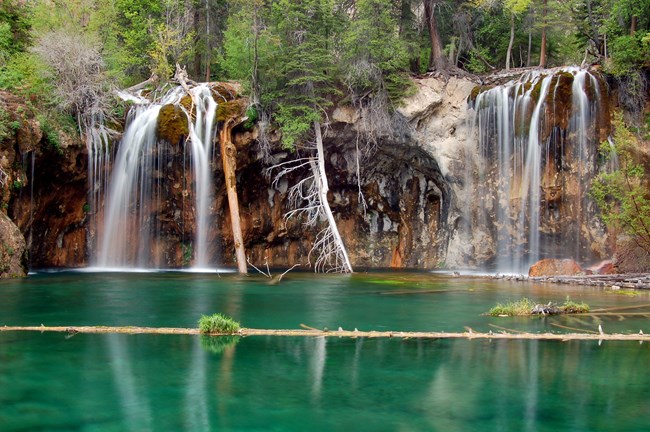 Green calm water in foreground with waterfall in background