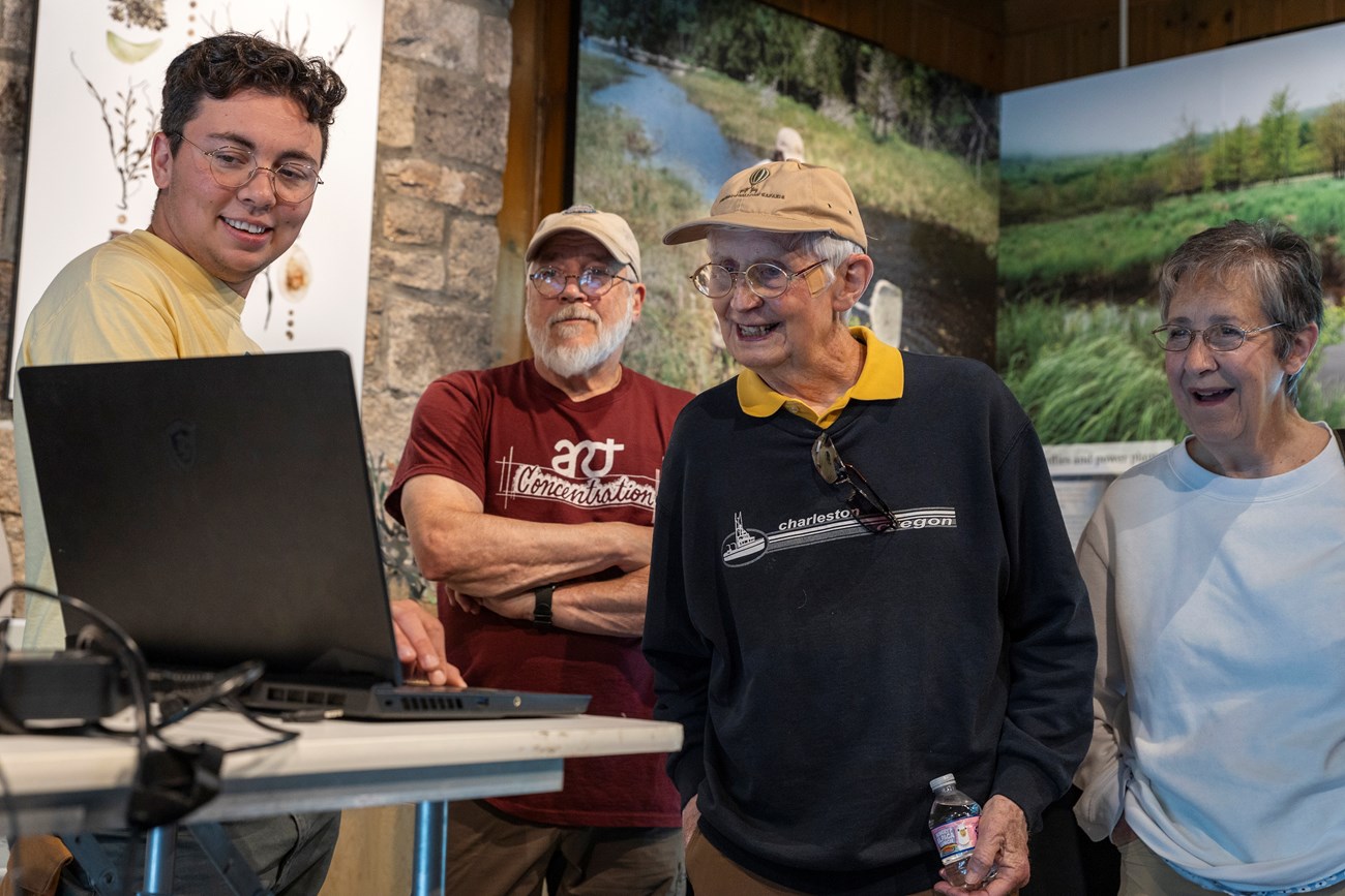 A man looks at a laptop while talking to a group of people