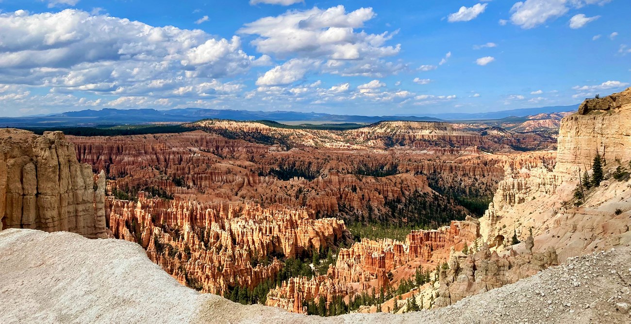 A vast landscape of irregularly shaped, orange and cream-colored rock formations under a blue sky with clouds.