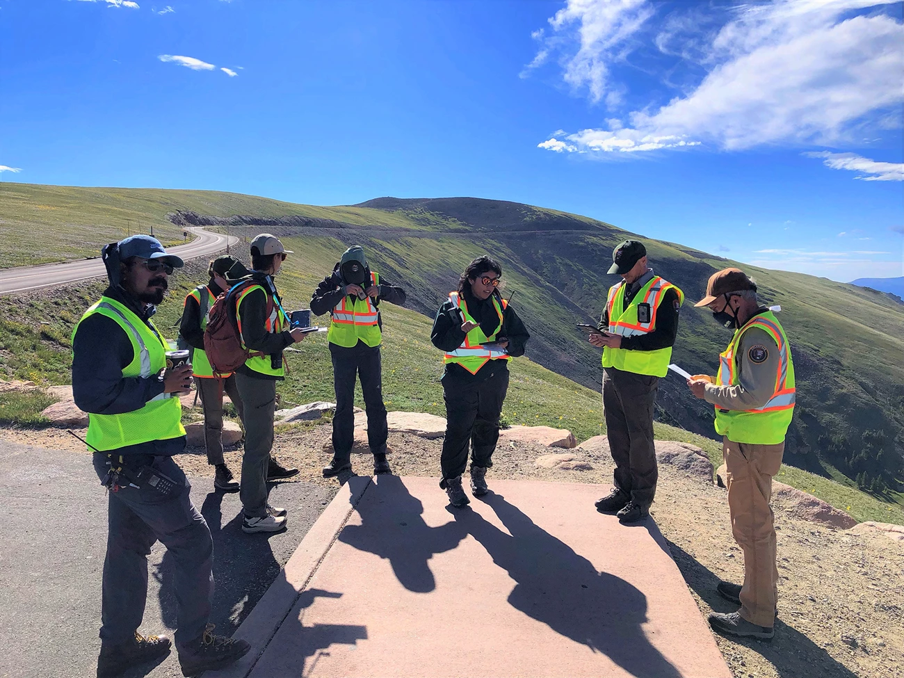 Park staff and citizen scientists A group of people in safety vests stand in a circle talking against an alpine backdrop