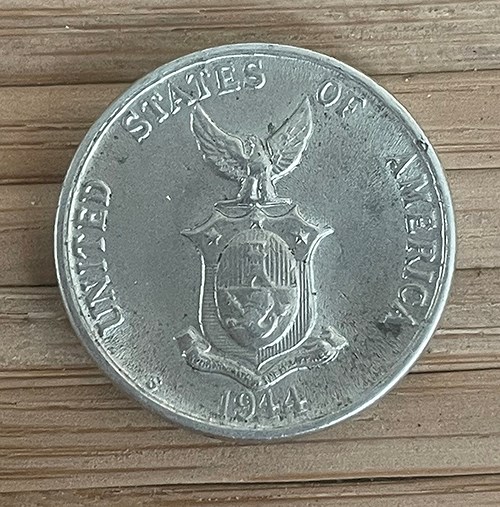 A silver colored coin with the coat of arms of the Philippine Commonwealth with an eagle and a shield. Words circling the coat of arms read: “UNITED STATES OF AMERICA / 1944.”  Collection of the Author