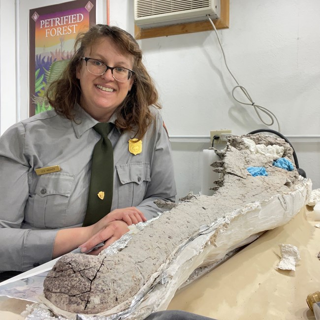 a ranger in uniform seated next to a large fossil