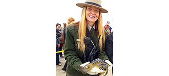 Shaver in uniform, lifting a sea turtle with white rubber gloves.