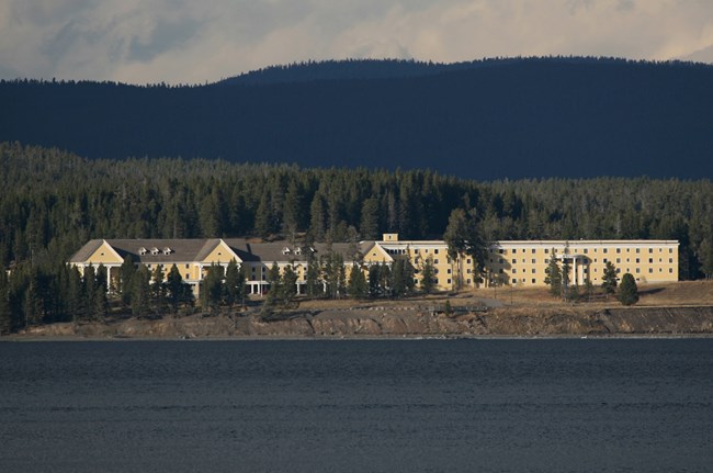 Figure 1 Photograph taken from the water of a large yellow hotel along a lake coastline. The blue lake is in the foreground and a forest is in the background.
