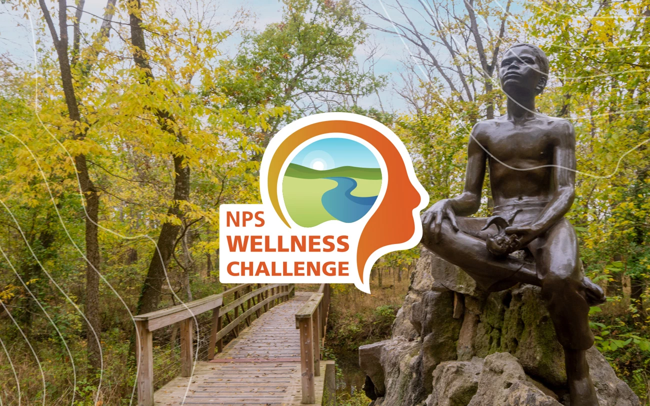 George Washington Carver Wellness Challenge Bronze statue of young George Washington Carver holding a plant and a foot bridge in the background.