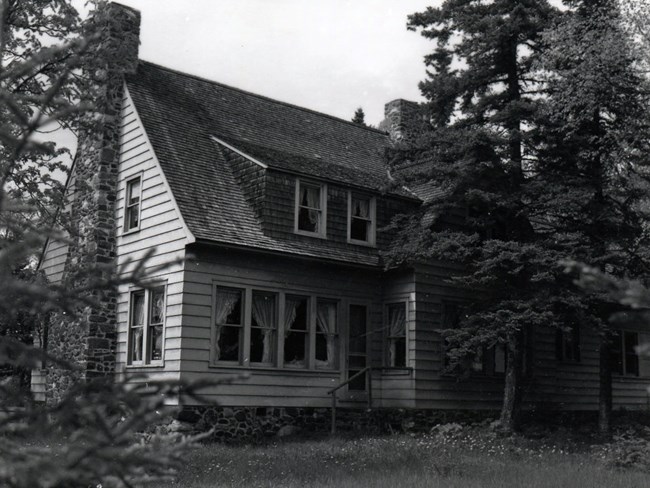 two story house with stone chimney, siding, stone foundation and many windows