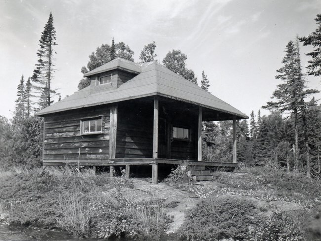 small square two level lock cabin, covered front porch very large compared to structure