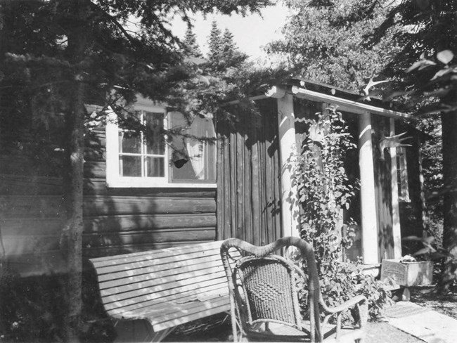 chairs in front of cabin, front window screen damaged with hole in it