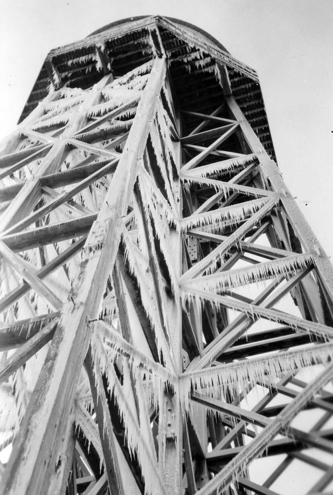 Masses of icicles cling to the rungs of water tower which looms over viewer.