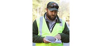 Flynn outside in a yellow safety vest looking at paperwork.