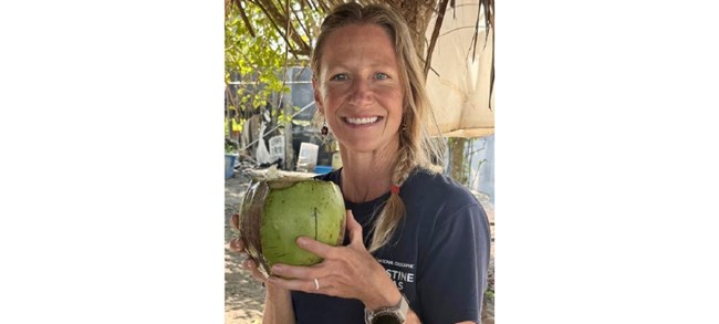 Moore smiling at the camera, holding a coconut to drink from.