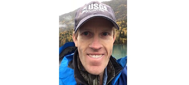 Legleiter smiling outside in a USGS ball cap in front of a scenic lake.