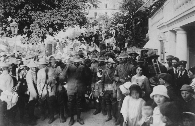 Link369thinFrance Soldiers, in uniform, surrounded by civilians, building visible at right