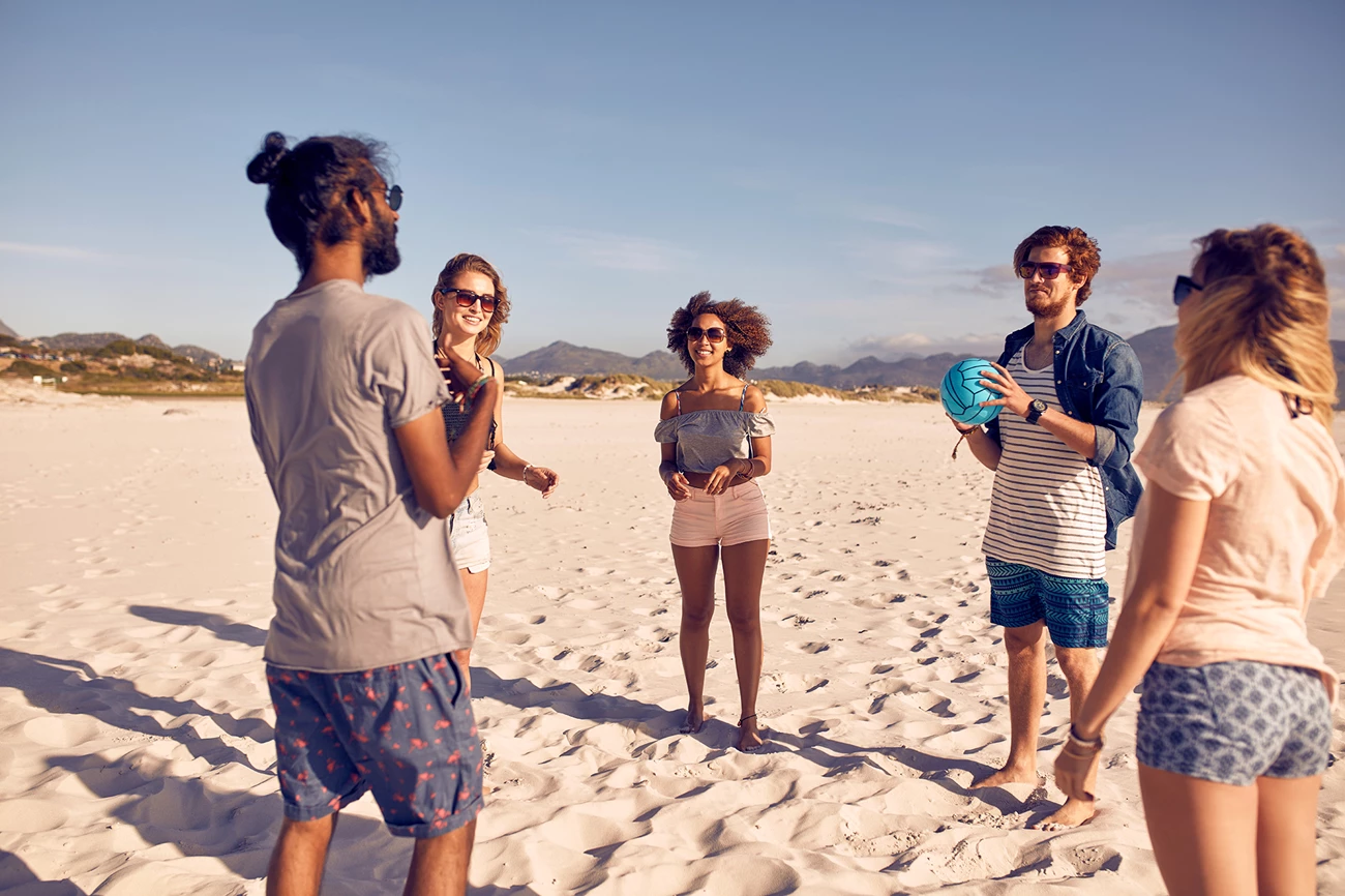 On the beach with a volleyball Five people stand on a beach, talking. One holds a volleyball.