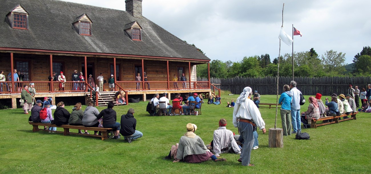 Many people gathered on a lawn in front of an historic building.