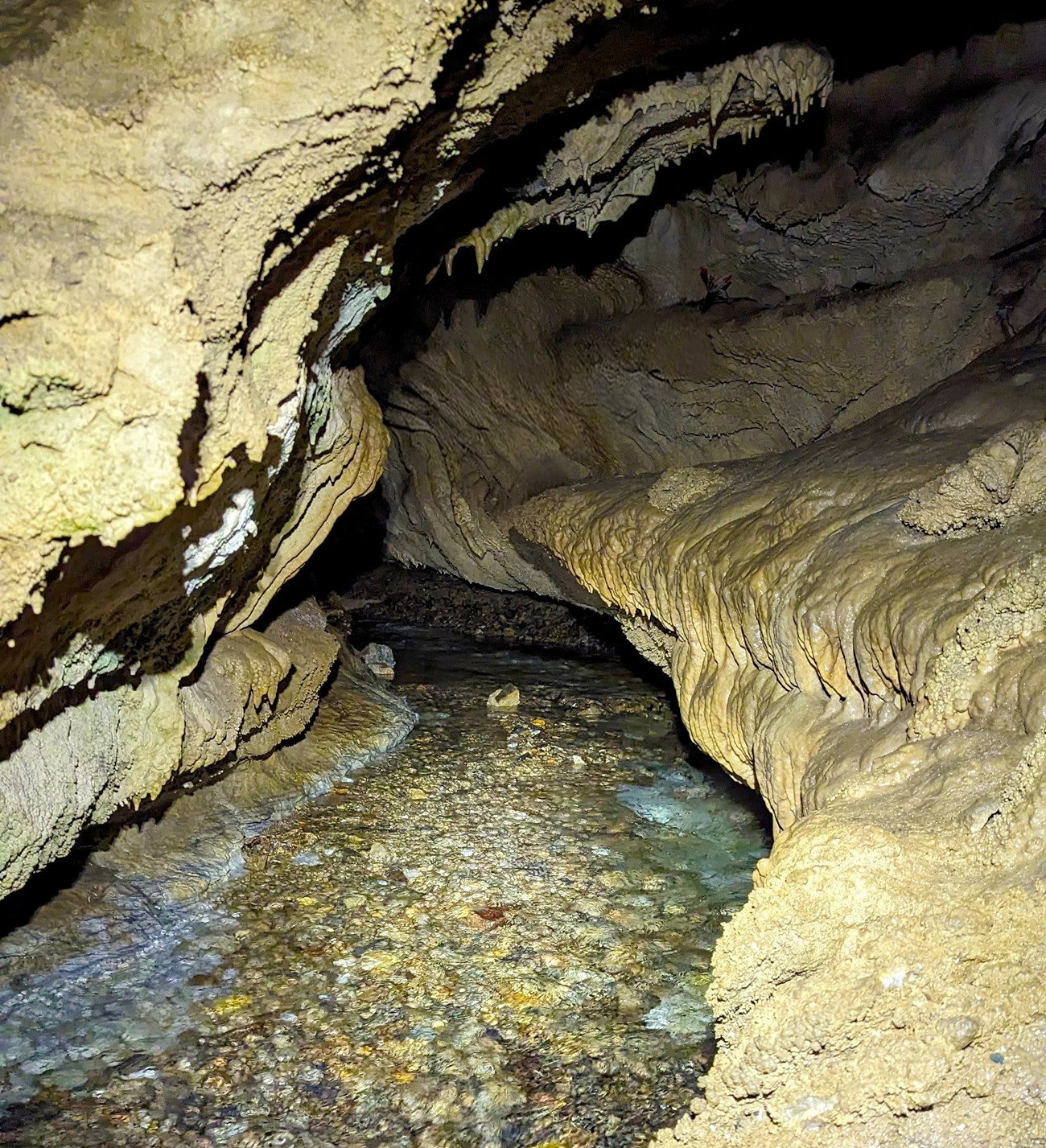 Cave passage lined with cave formations follows the River Styx as it bends out of sight.