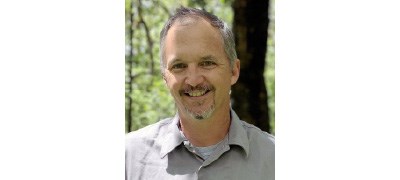 Headshot of Seth Judge outside in a forest, wearing a gray collared NPS shirt.