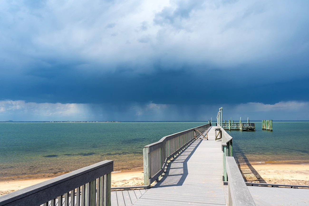 Storm clouds on the horizon A photo of a gray dock stretching out into blue-green water, with a storm approaching.