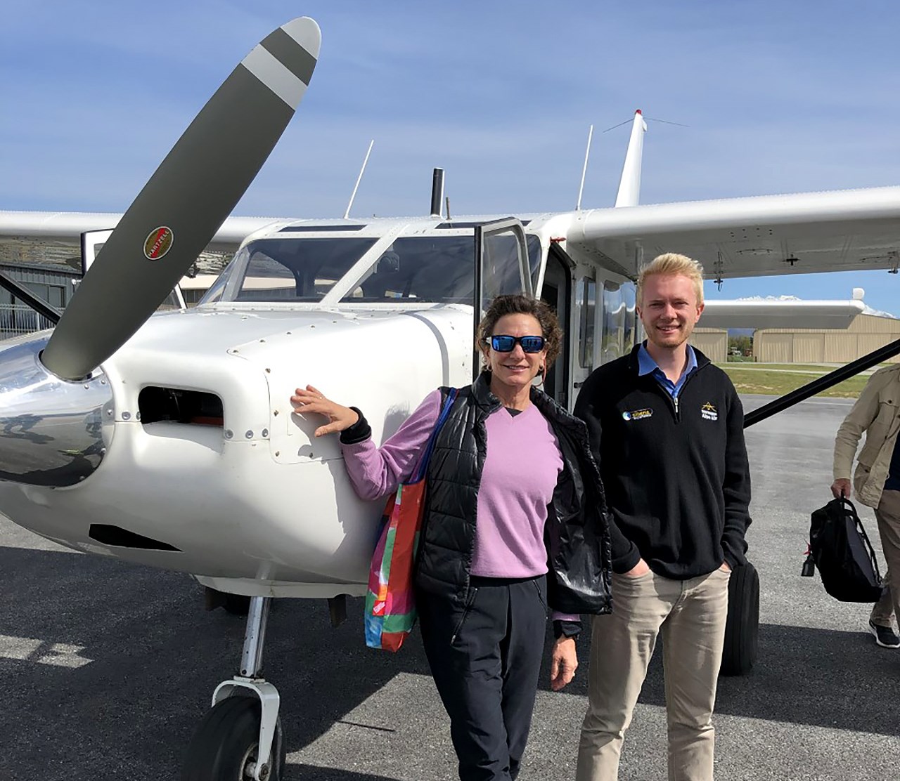 A man and a woman stand in front of a small airplane on the tarmac