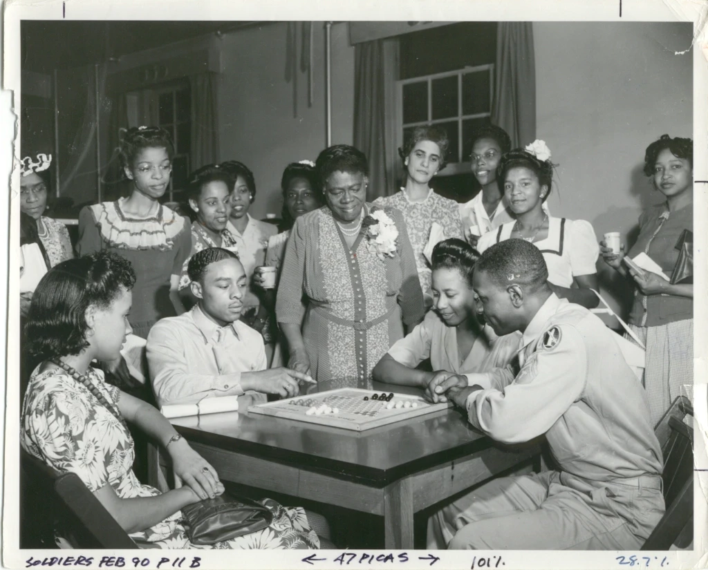 African American USO, early 1940s African American USO, early 1940s. Pictured is a group of people playing a board game on a table.