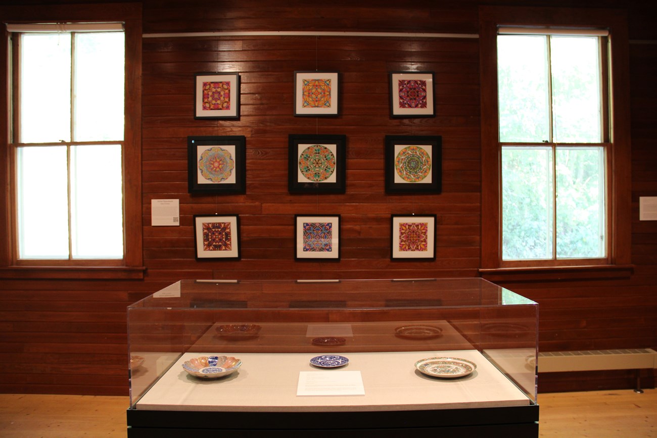 Nine framed geometric art pieces in background with case of plates in the foreground