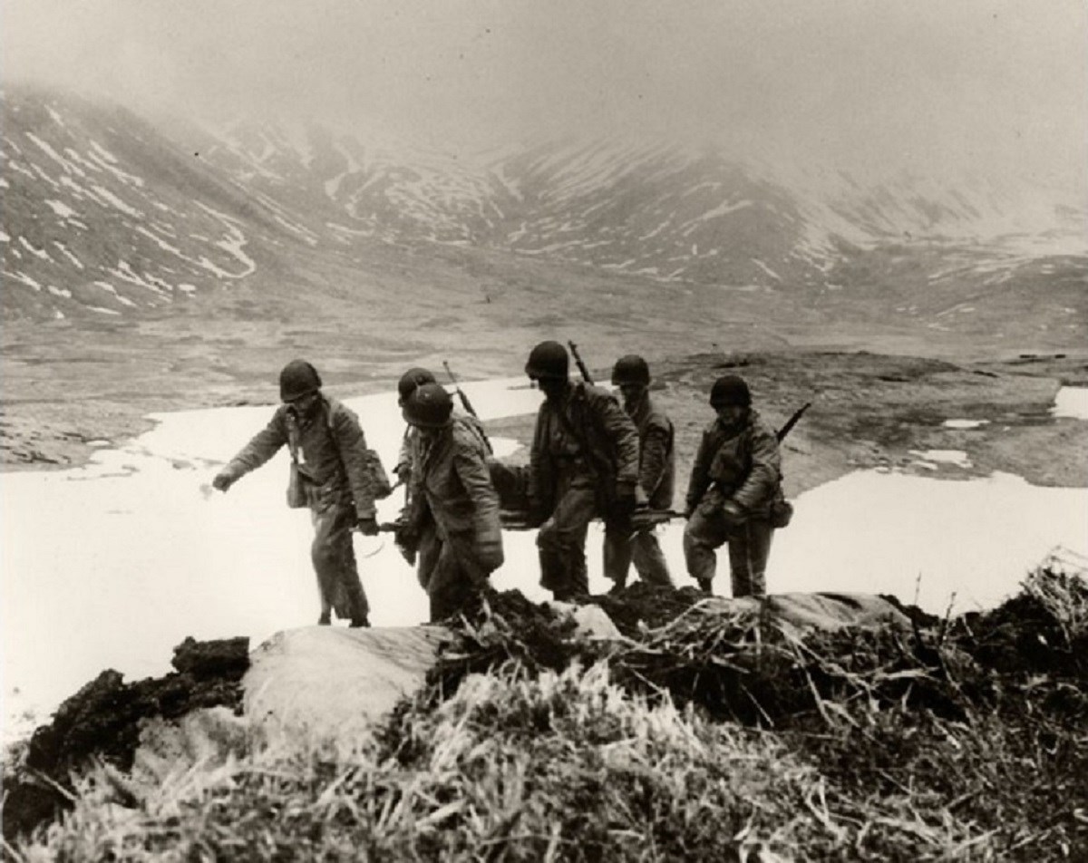 black and white photo of six soldiers carrying wounded person on stretcher.