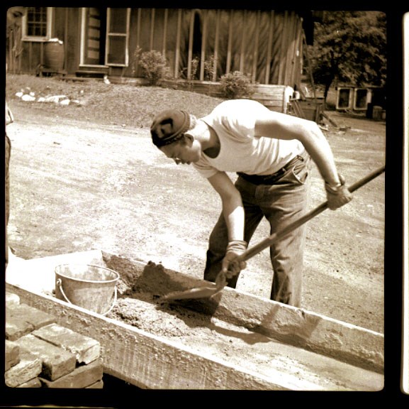 A man in white tshirt uses a shovel