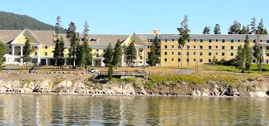Yellow hotel Photo taken from the lake of a large yellow hotel and road between the hotel and the water. A wooden viewing platform rests on top of a sandy bluff close to the edge. Water is in the foreground.