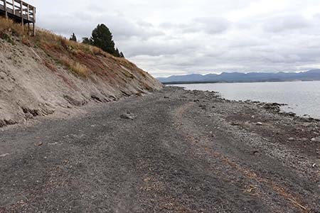 View of the bluff area of concern View looking down a tan and grey sand shoreline. In the left of a frame is the coastal bluff and to the right is a lake.