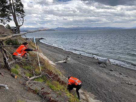image010Mod Two people wearing orange vests take measurement along a coastal bluff that is covered in light vegetation and debris. A lake is in the backround.