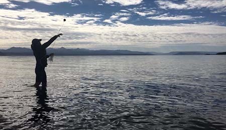 image10Mod Silhouette of a person standing in a lake throwing a Sonobuoy into the water. The Sounobuoy looks like a small ball with a string attached.