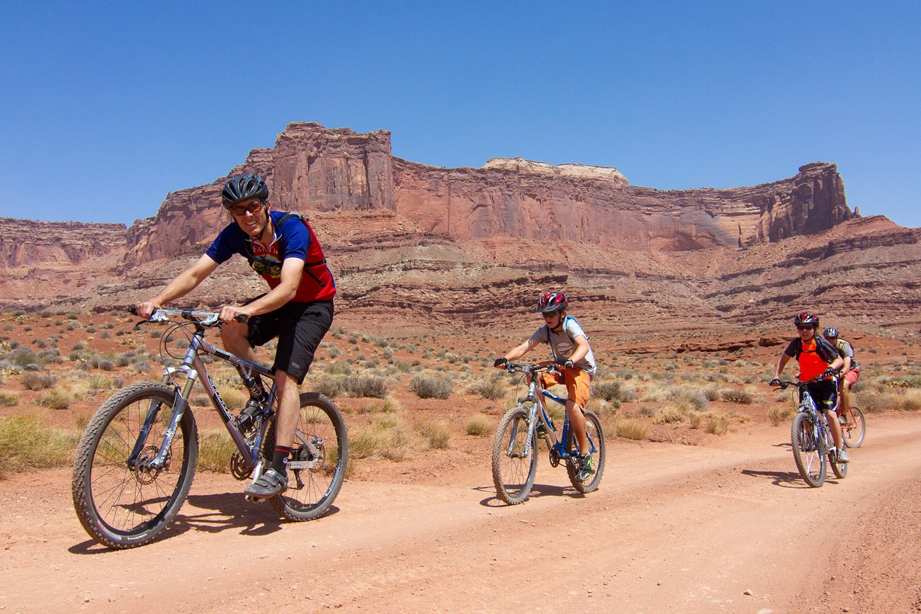 mountain biking four mountain bikers with helmets and packs bike down a dirt trail in the desert
