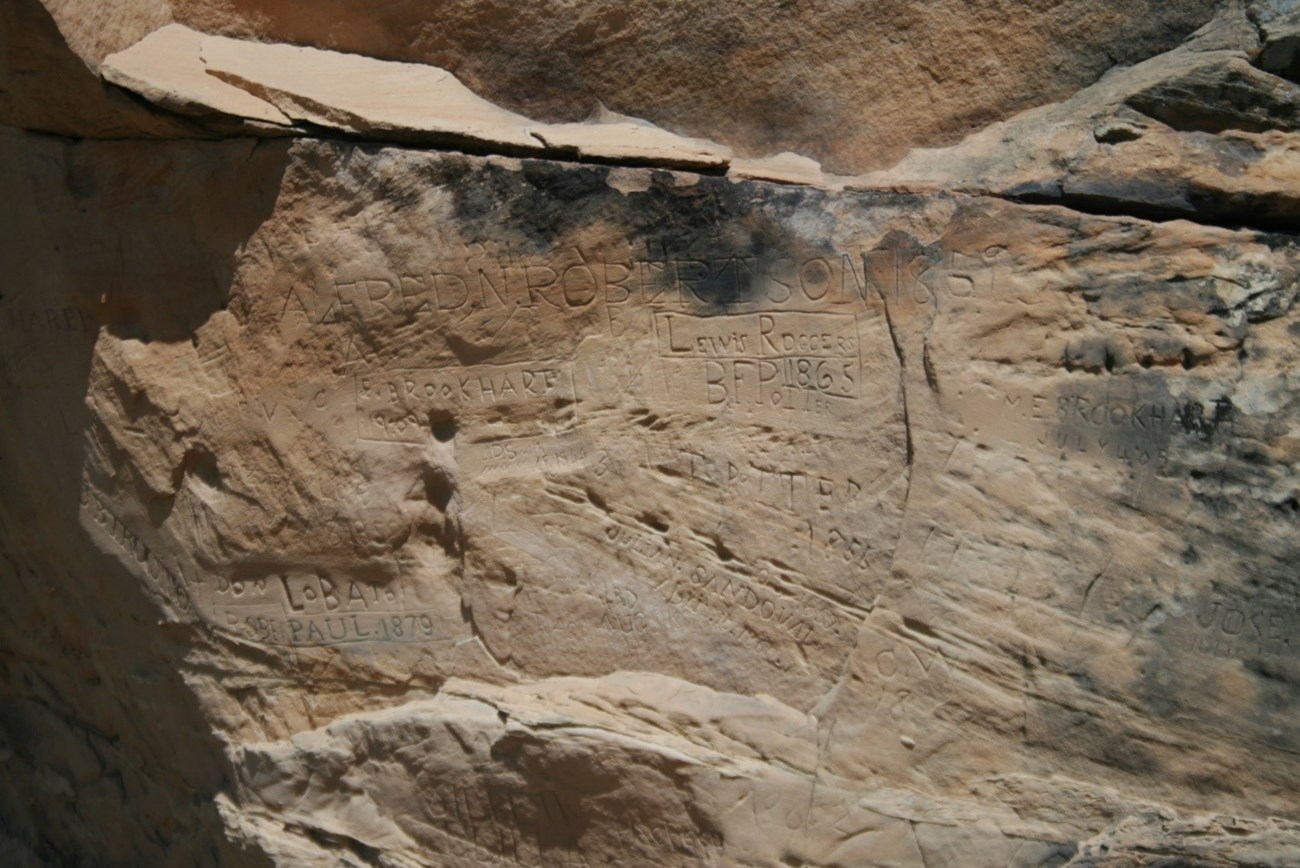 lt= Rock formation with names and dates carved into it.