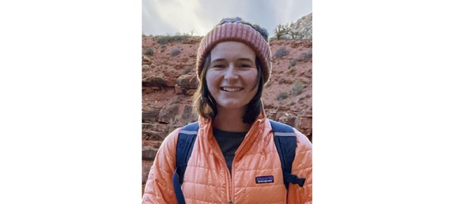 Brooke Bauman Bauman in a warm jacket, hat, and backpack, smiling in front of a canyon.