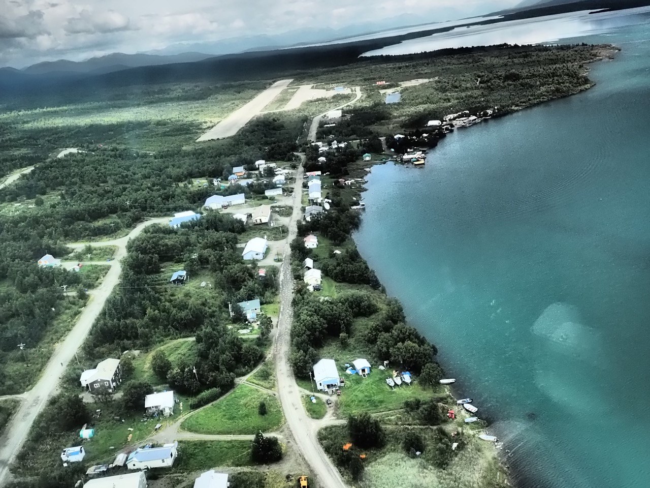 An aerial view of Nondalton, shows small homes and roadways next to lush green grass, and turquoise water.