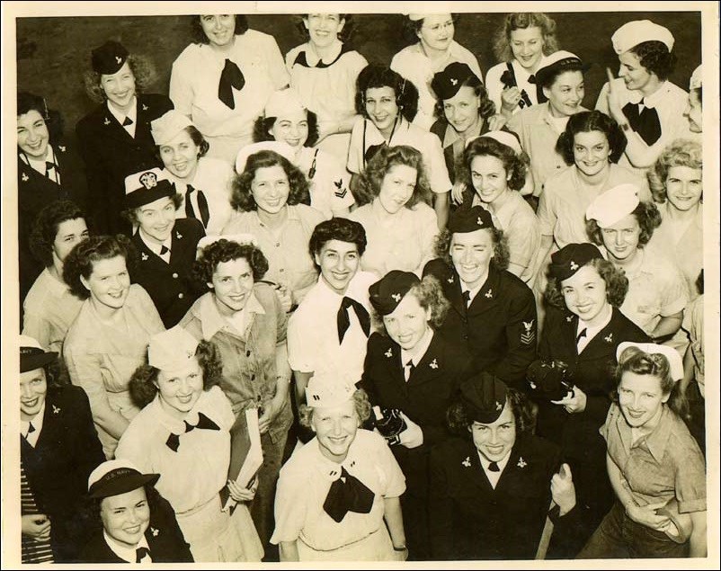 Women standing and smiling for photo, displaying objects associated with their jobs, NAS New York, 1945.