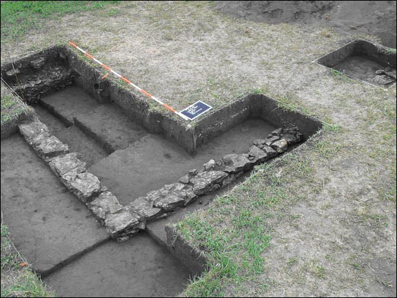 Photo of an archaeological excavation with square excavation units revealing part of a wall made of stone. (Photo by Paul A. Shackel)