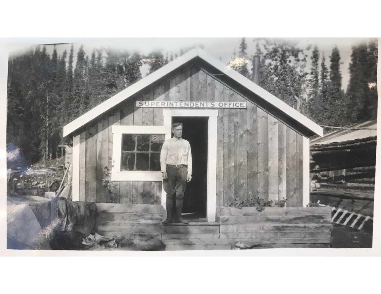 man standing outside a small wooden building in a forest